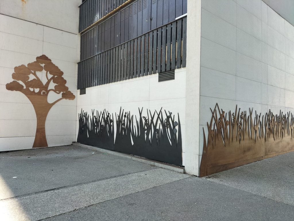 habillage soubassement immeuble avec fresque en bois représentant un arbres et des herbes hautes